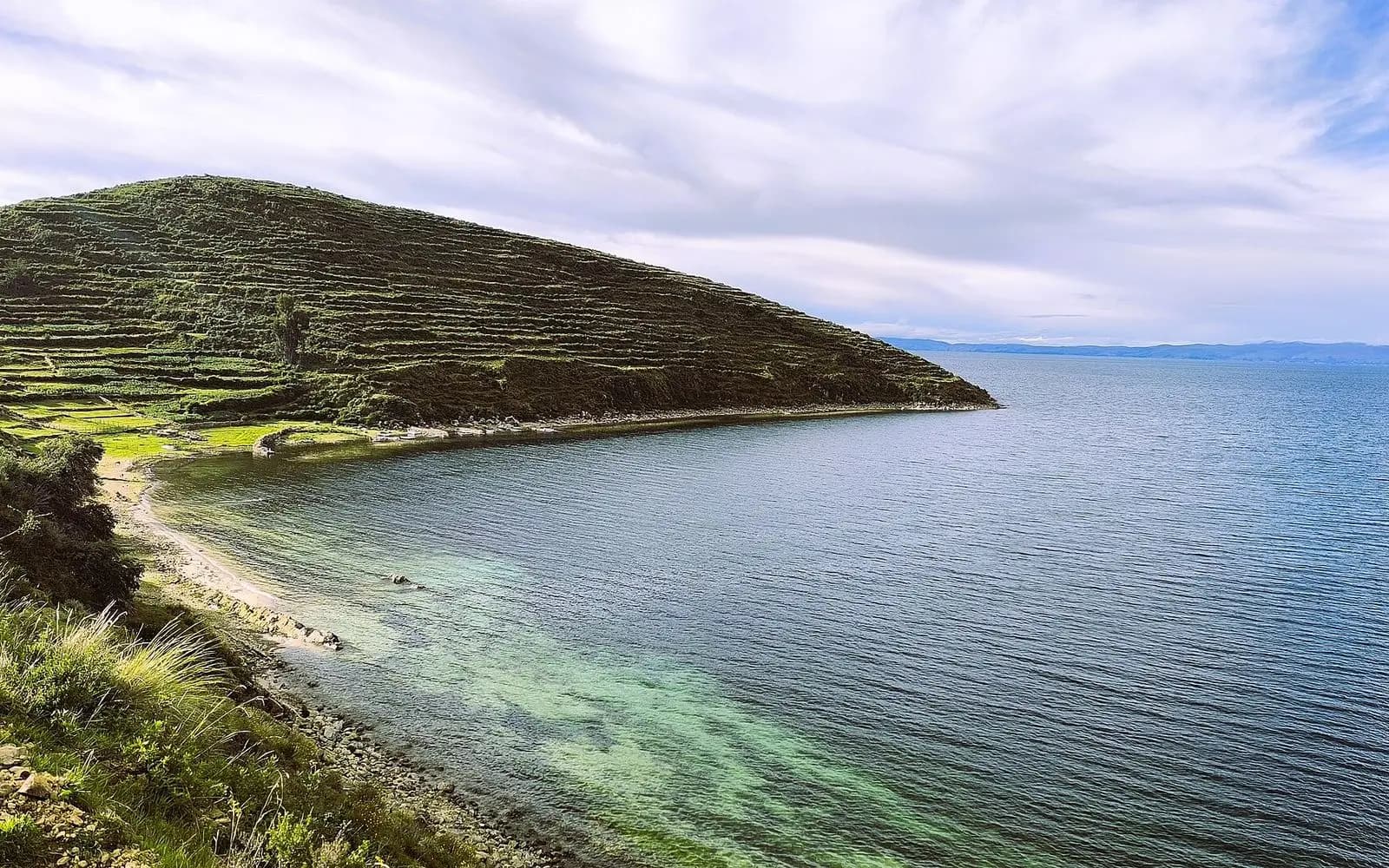Terraced green headland and turquoise shallows of Lake Titicaca on Isla del Sol, La Paz, Bolivia