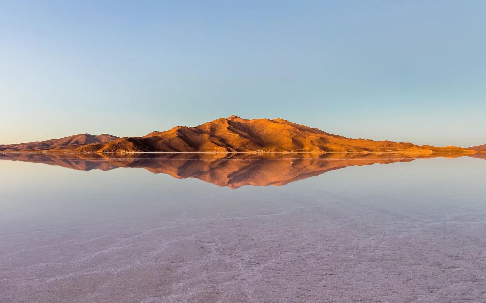 Mirror-like water on the Salar de Uyuni reflecting an orange island at sunrise, Potosí, Bolivia