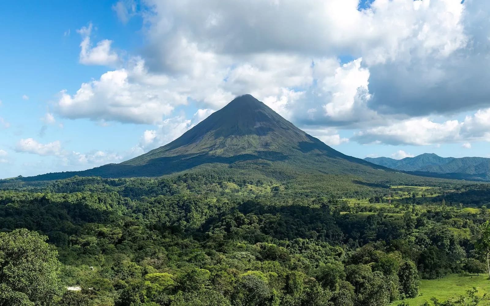 Arenal Volcano's perfect cone rising above green rainforest under scattered clouds, Arenal, Costa Rica