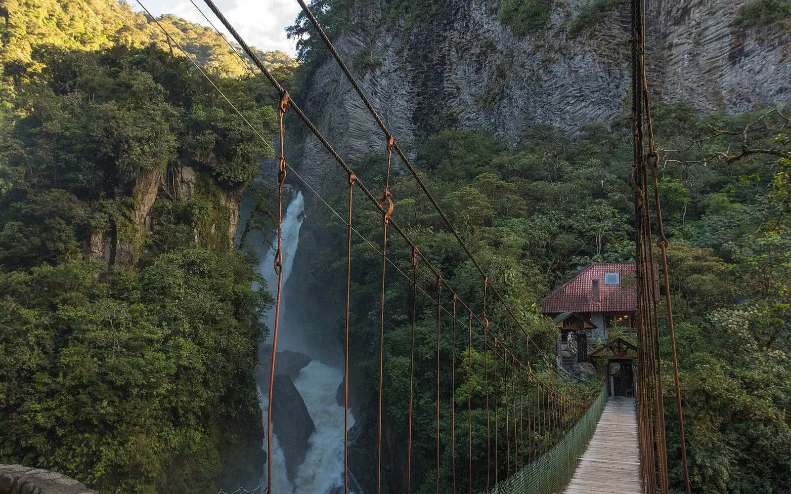 Suspension footbridge leading to the Pailón del Diablo waterfall in lush green gorge, Baños, Ecuador