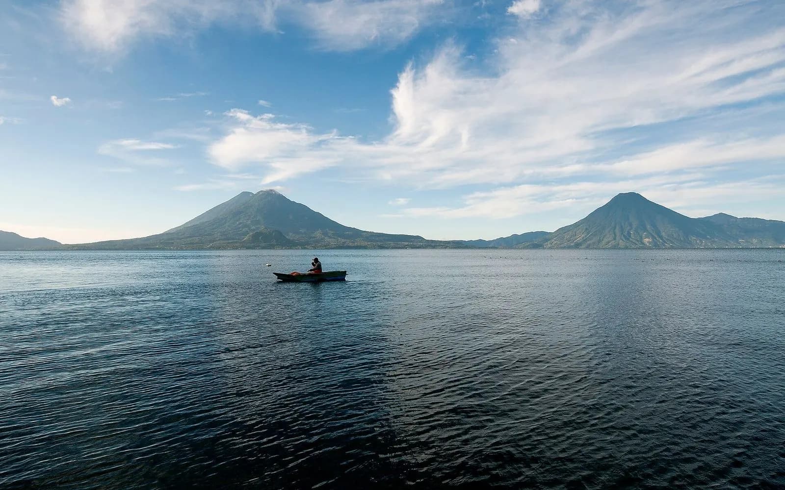 Two volcanoes rising above calm Lake Atitlán with a lone boat, Lake Atitlán, Guatemala