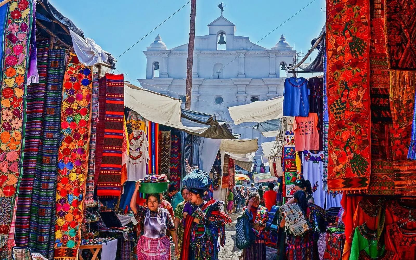 Colourful textile stalls with the white church behind at the market, Chichicastenango, Guatemala