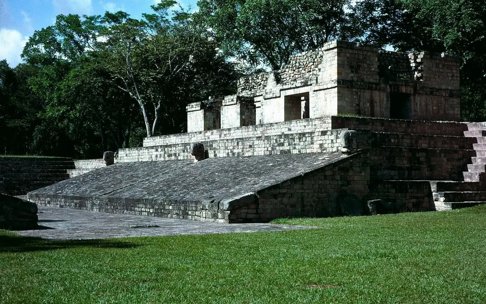 Stone ball court and temple structure above a green lawn at the Maya ruins, Copán, Honduras
