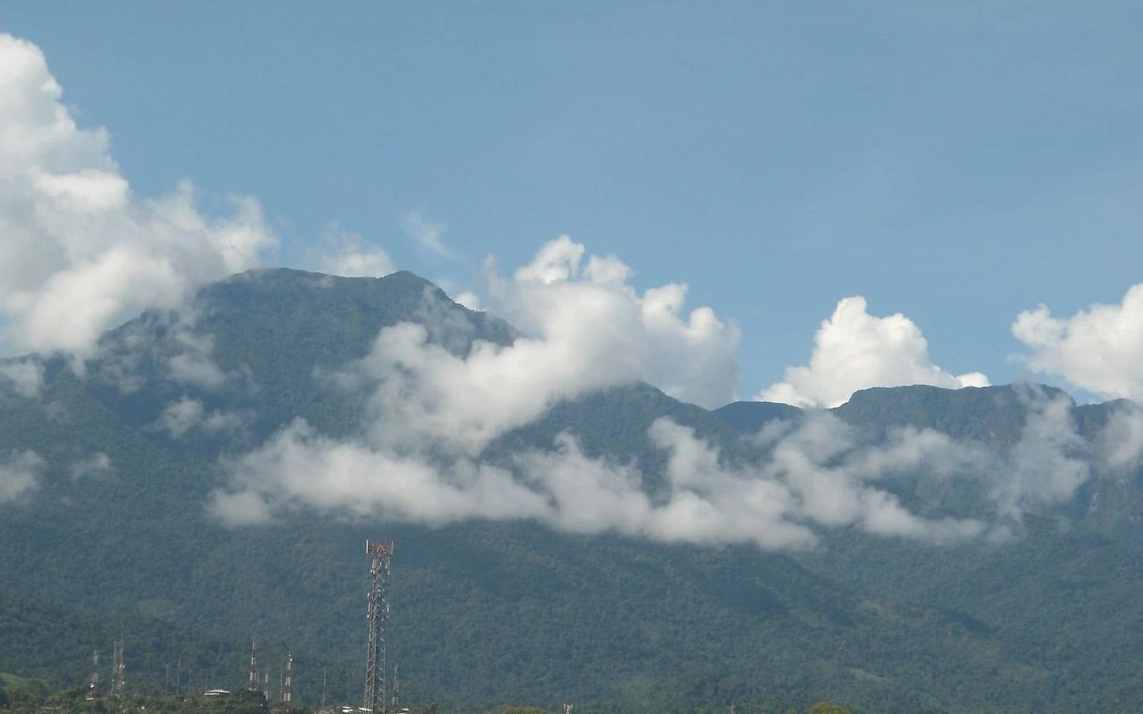 The forested Pico Bonito mountain range wrapped in clouds under a blue sky, Pico Bonito, Honduras