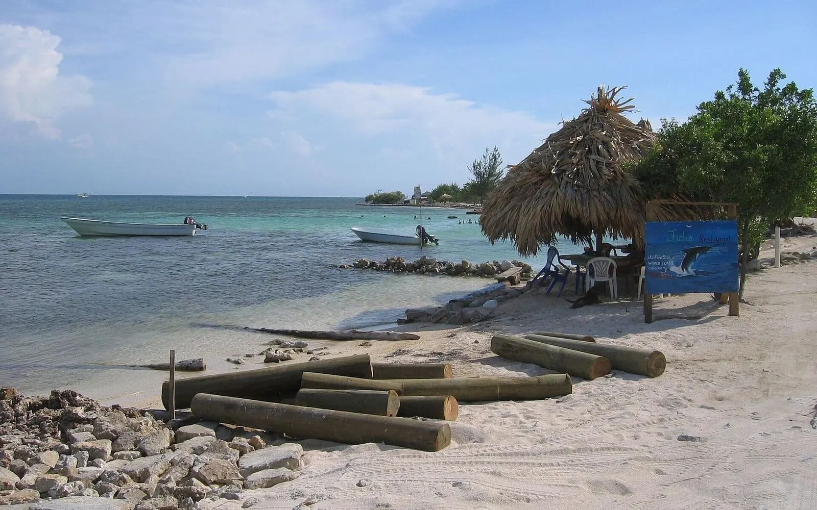 Thatched palapa and small boats on a sandy beach by turquoise water, Utila, Honduras