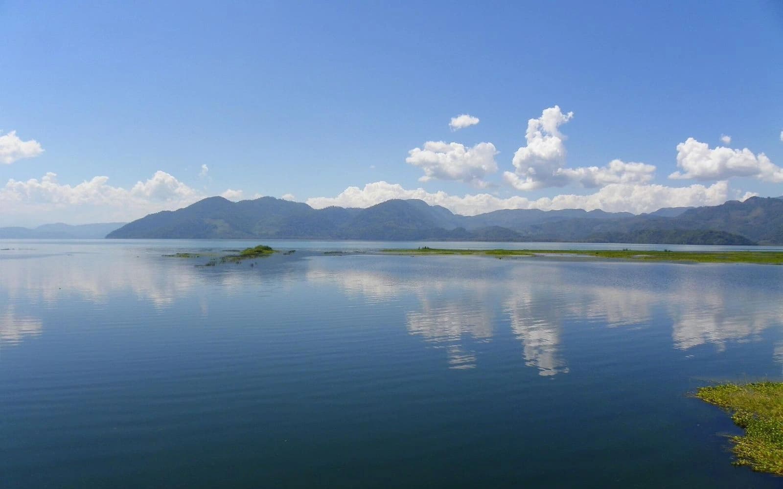 Calm blue water reflecting clouds with green mountains beyond at Lake Yojoa, Honduras