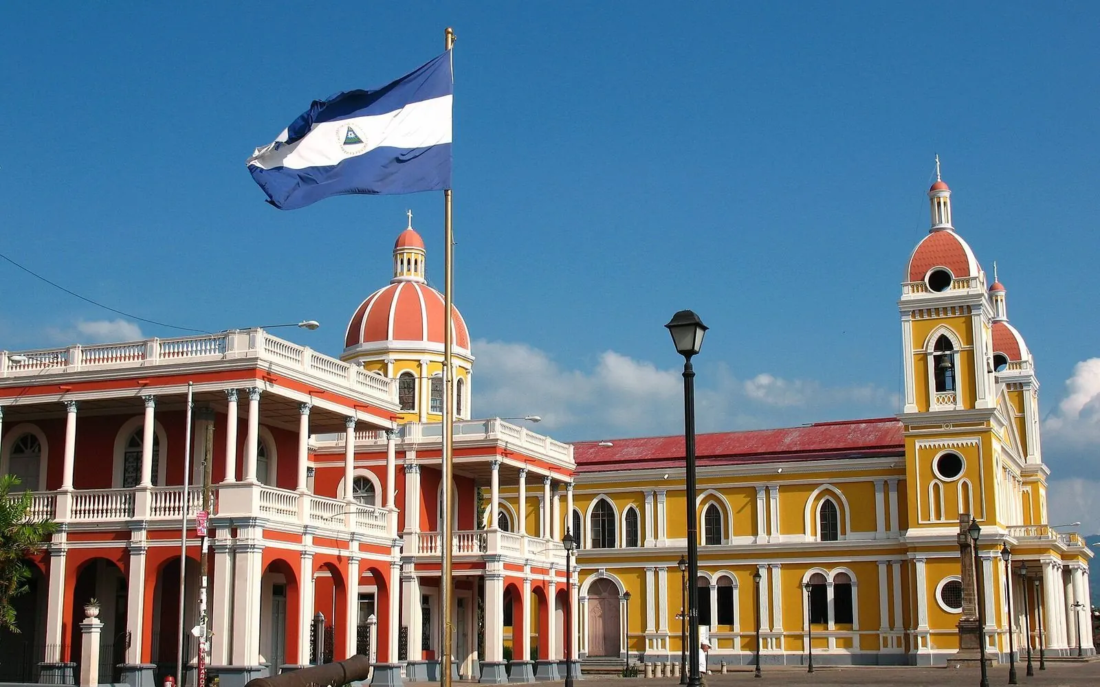 Yellow cathedral and a red colonial building with the national flag, Granada, Nicaragua