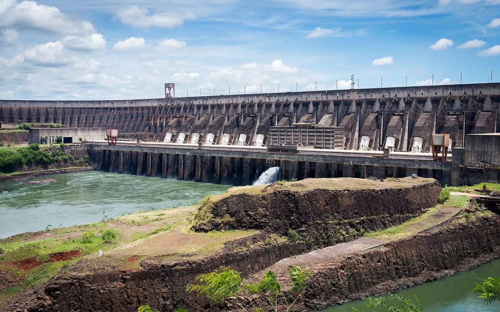 The curved concrete wall of Itaipú Dam above the river with water spilling out, Paraguay