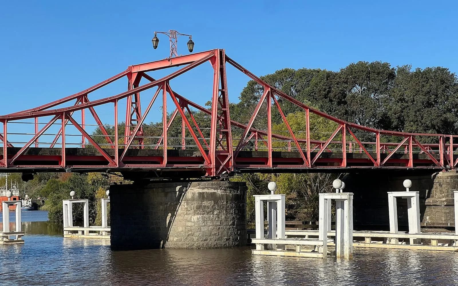 Red steel swing bridge with white mooring posts over the river, Carmelo, Uruguay